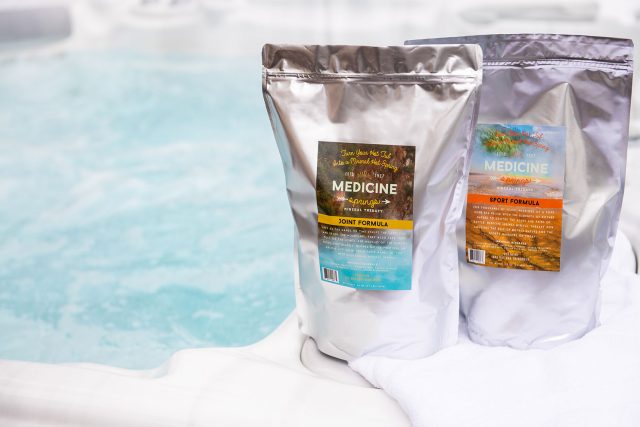 Two pouches of Medicine Springs product. These are the Joint Formula and Sport Formula mineral therapy sitting on the edge of a hot tub.